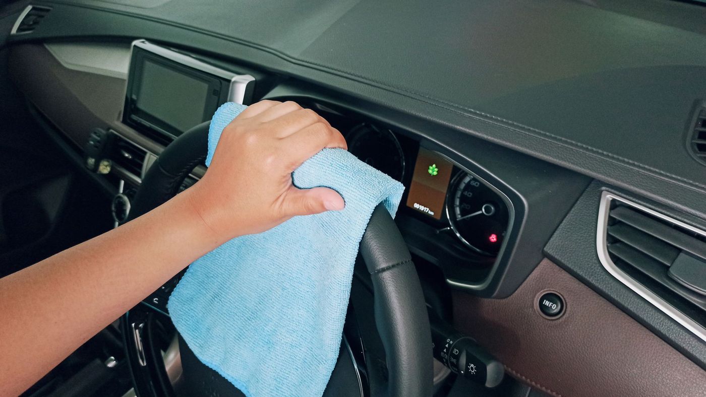 A hand wiping down a car steering wheel with a microfibre cloth. Stock photograph, not Uriel Detailing.