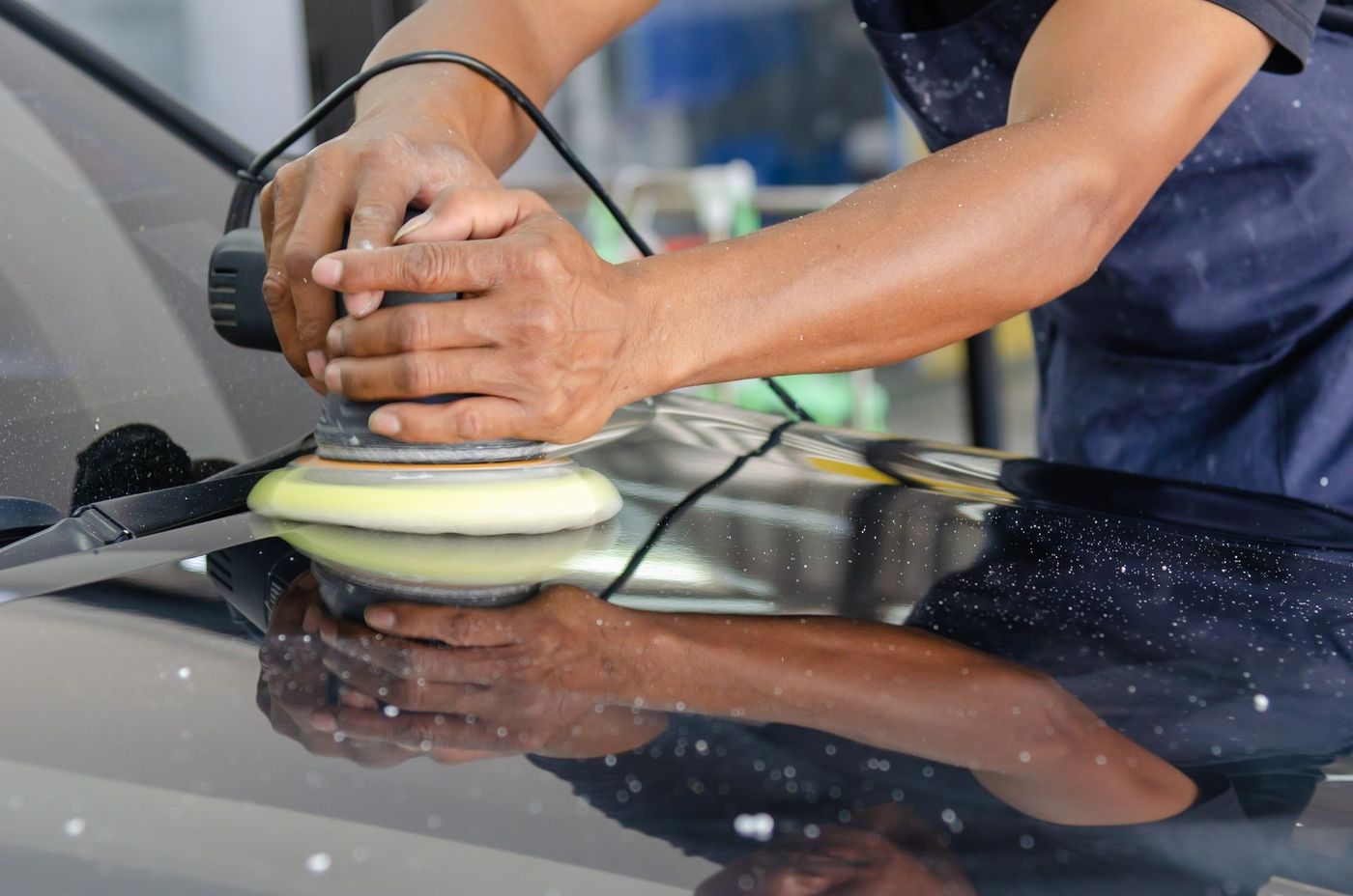 A machine polisher being worked across a dark car panel. Stock photograph.